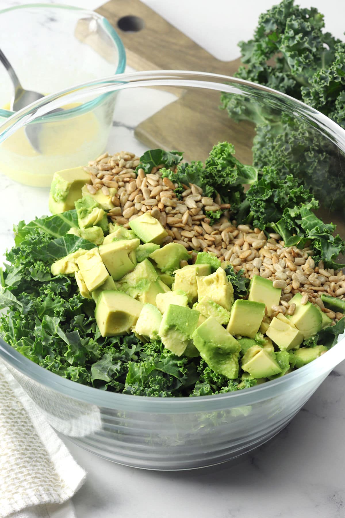 Chopped kale, avocado, and sunflower seeds in a large glass bowl.