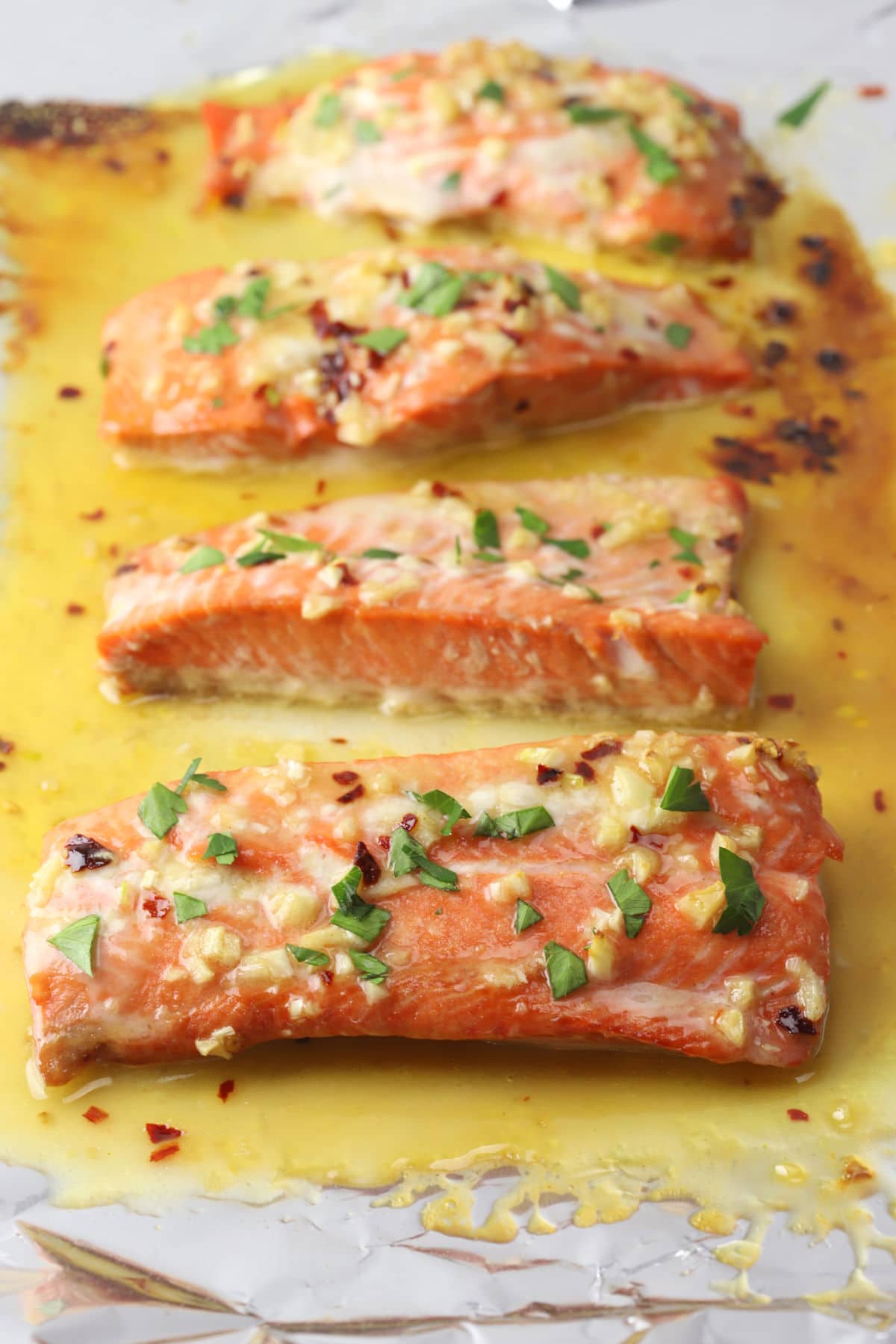 Salmon fillets topped with garlic and parsley sitting in butter sauce.