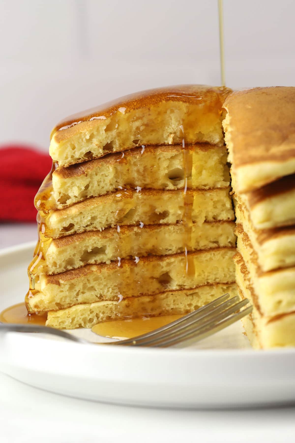 Maple syrup being poured over a stack of sliced buttermilk pancakes on a white plate.