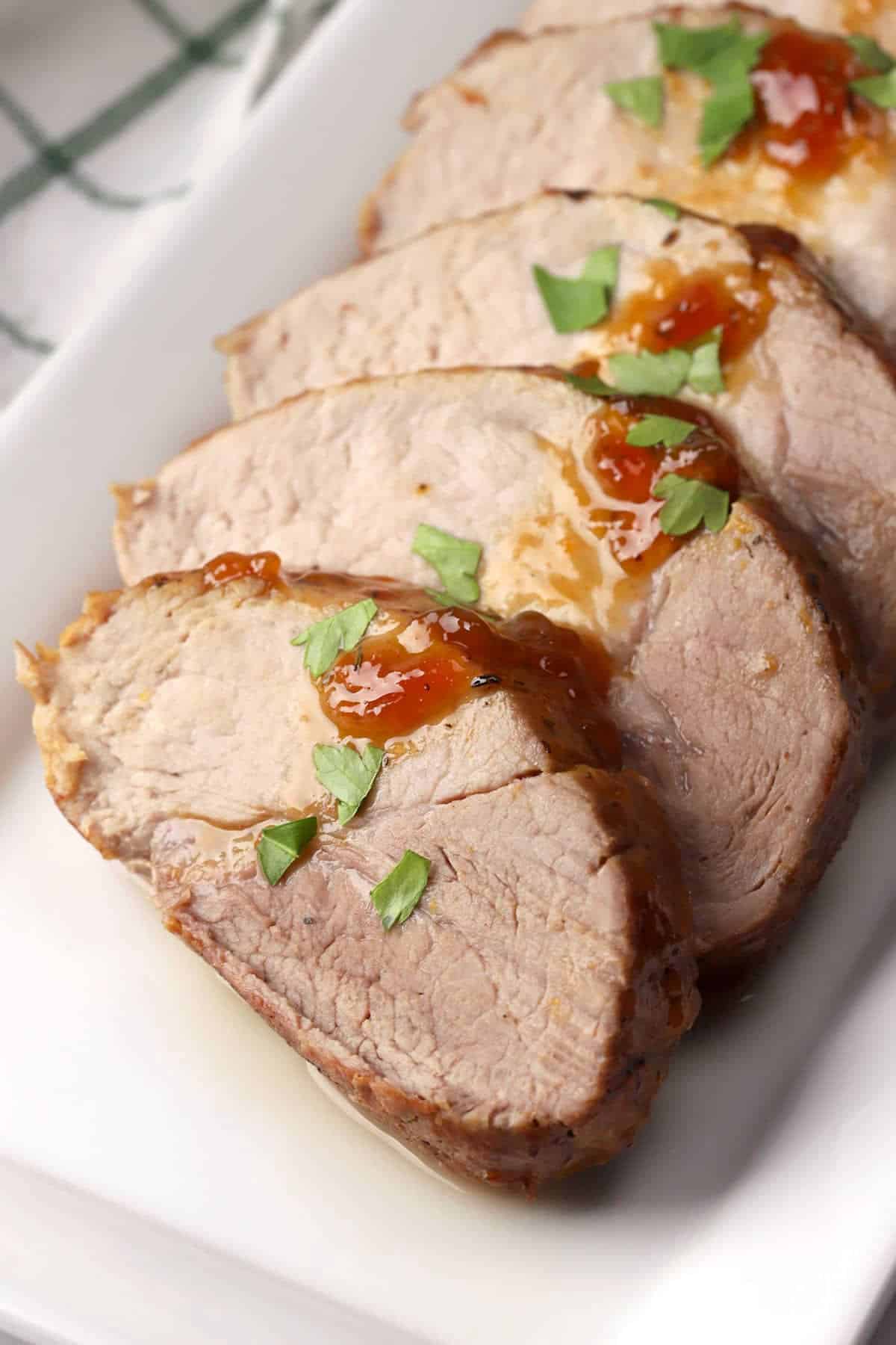 Sliced oven roasted pork loin on a white serving plate.