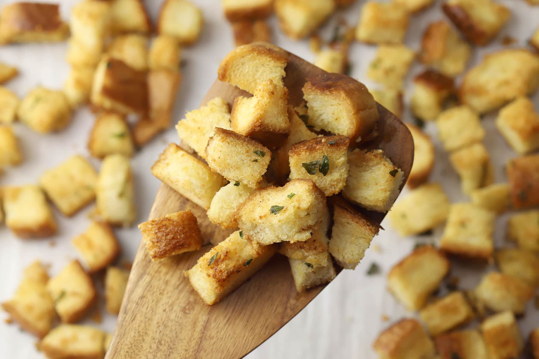 Wooden spatula scooping croutons from a baking sheet.
