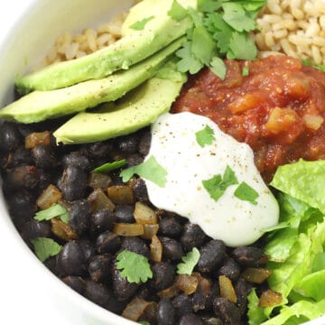 Close up of seasoned black beans, sliced avocado, lettuce, rice, salsa, and sour cream in a white bowl.