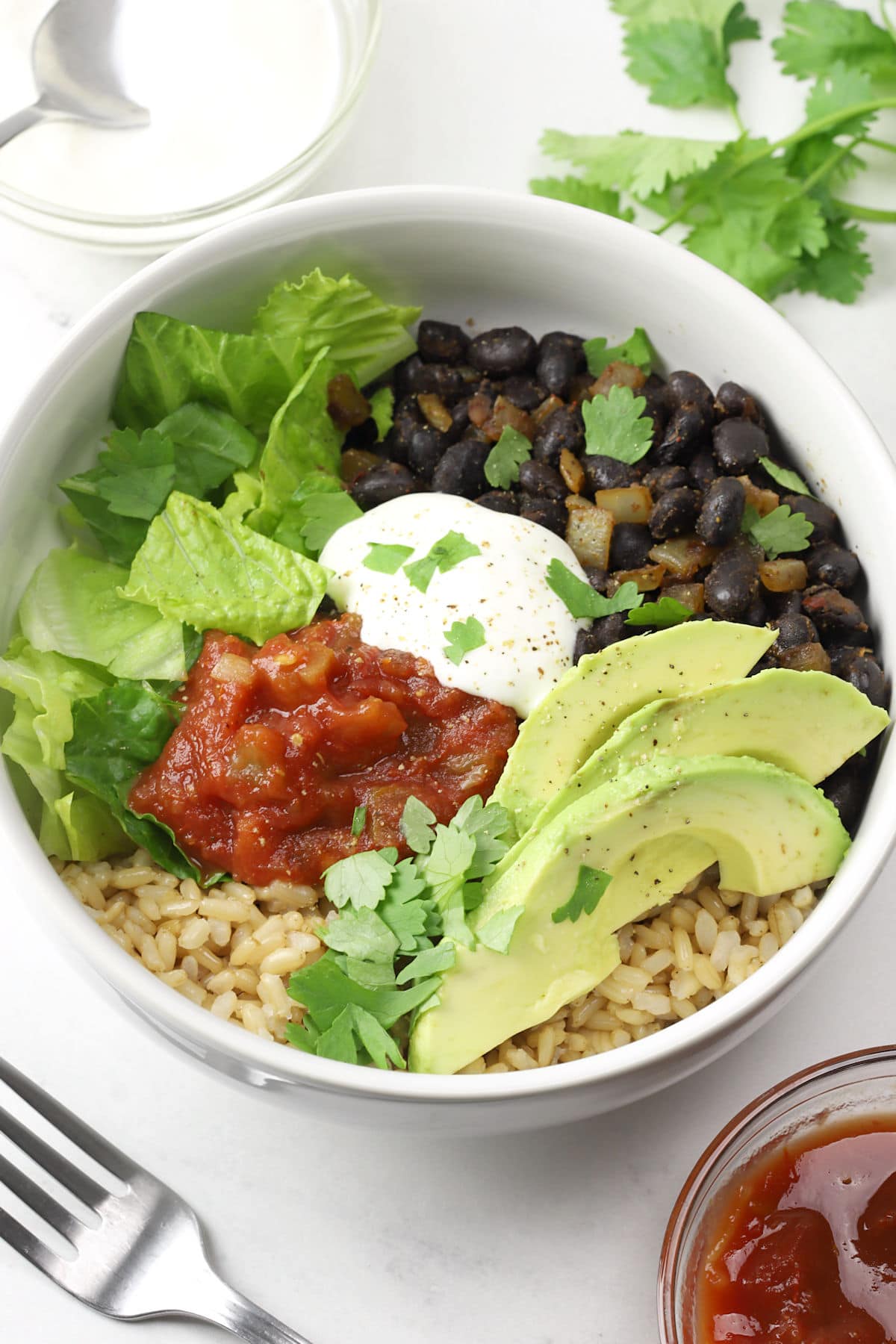White bowl filled with black beans, rice, and burrito toppings.