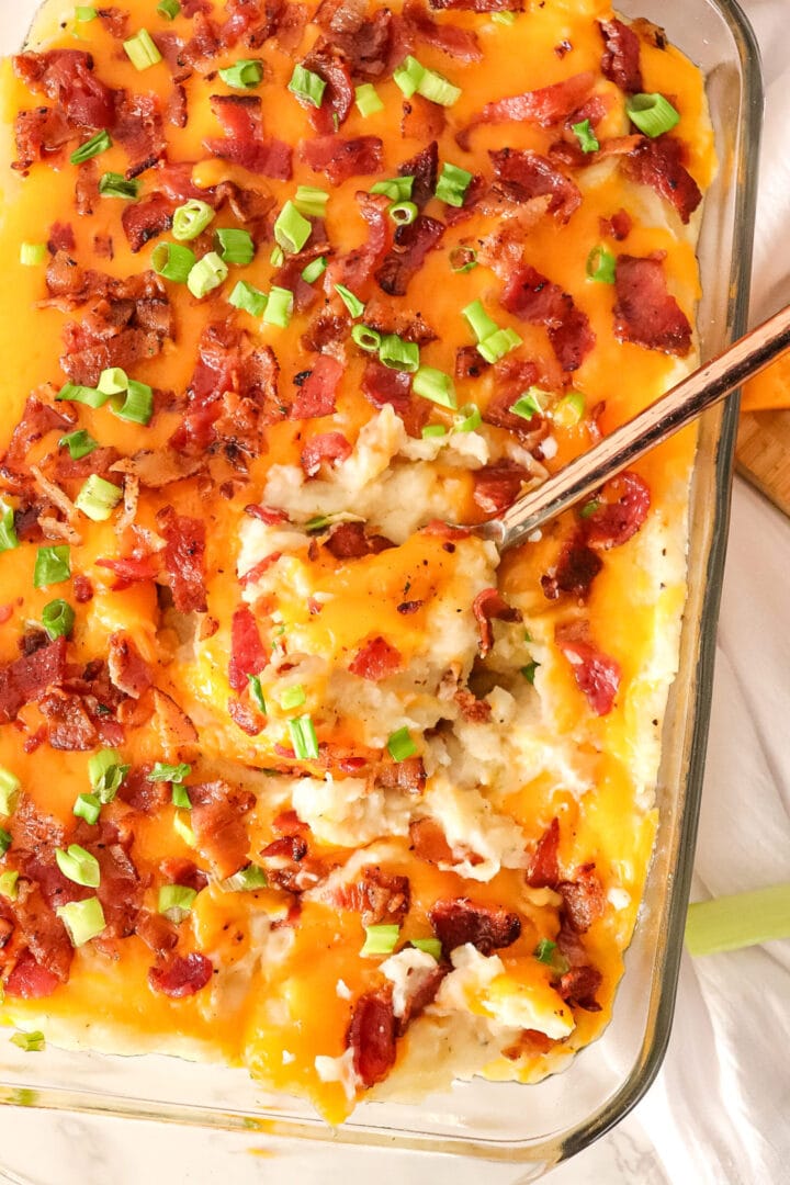 Glass casserole dish filled with mashed potatoes, cheese, and bacon.