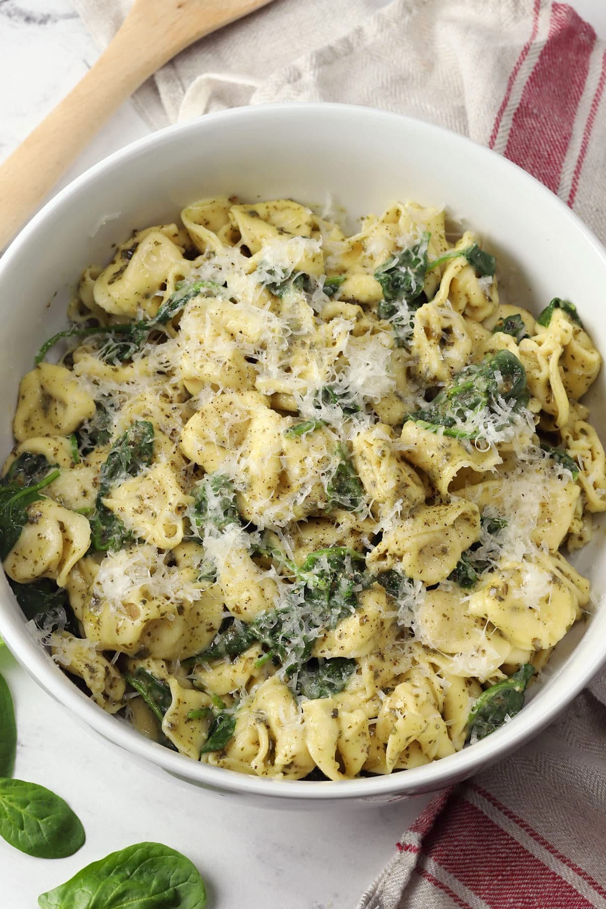 A large white bowl filled with pesto tortellini topped with shredded parmesan cheese.