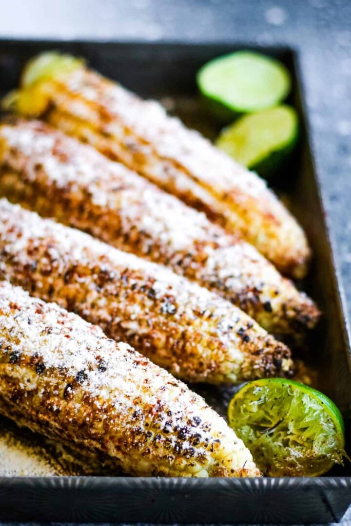 Grilled corn in a baking pan with grilled limes.