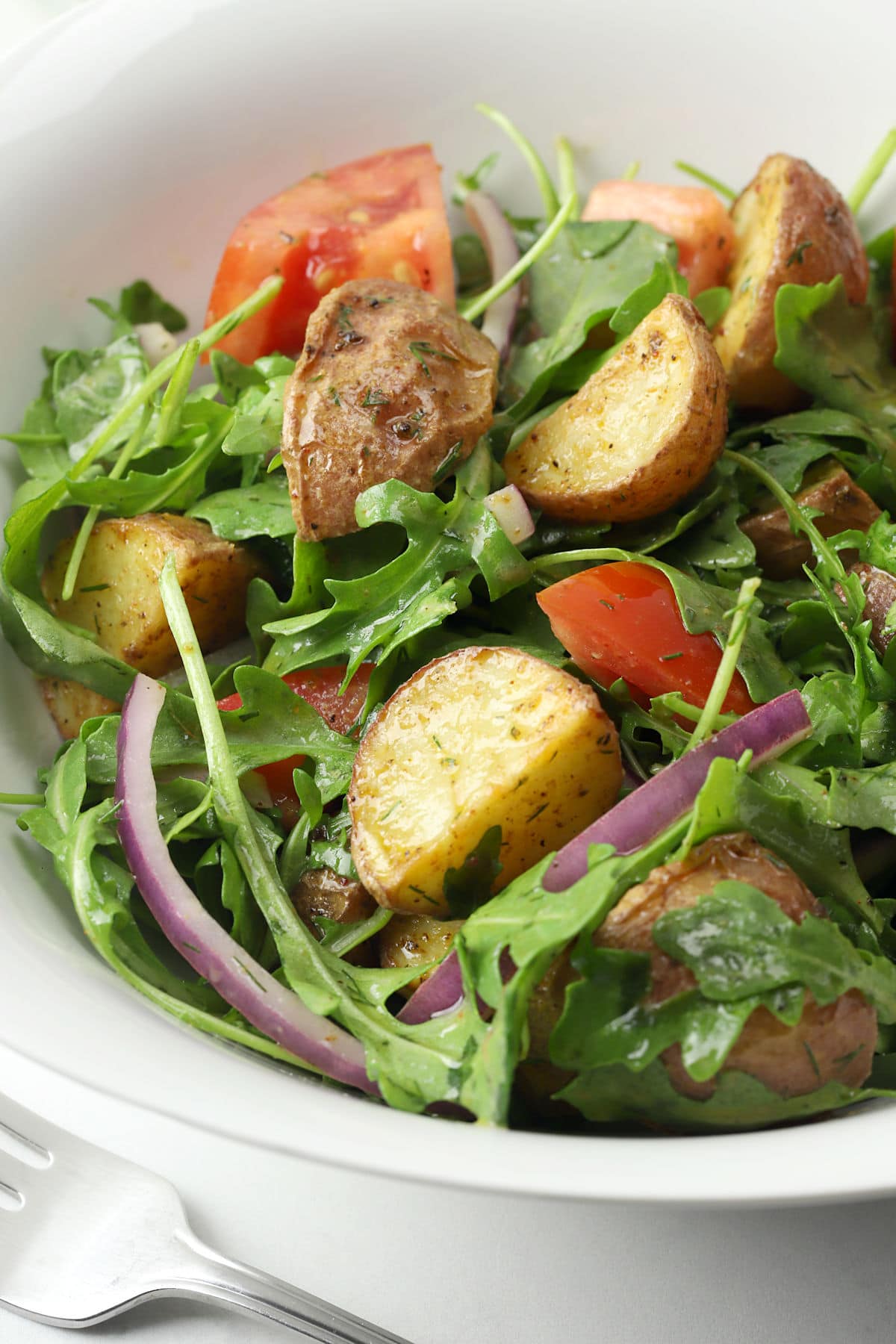 Roasted potatoes tossed in an arugula salad in a white bowl.