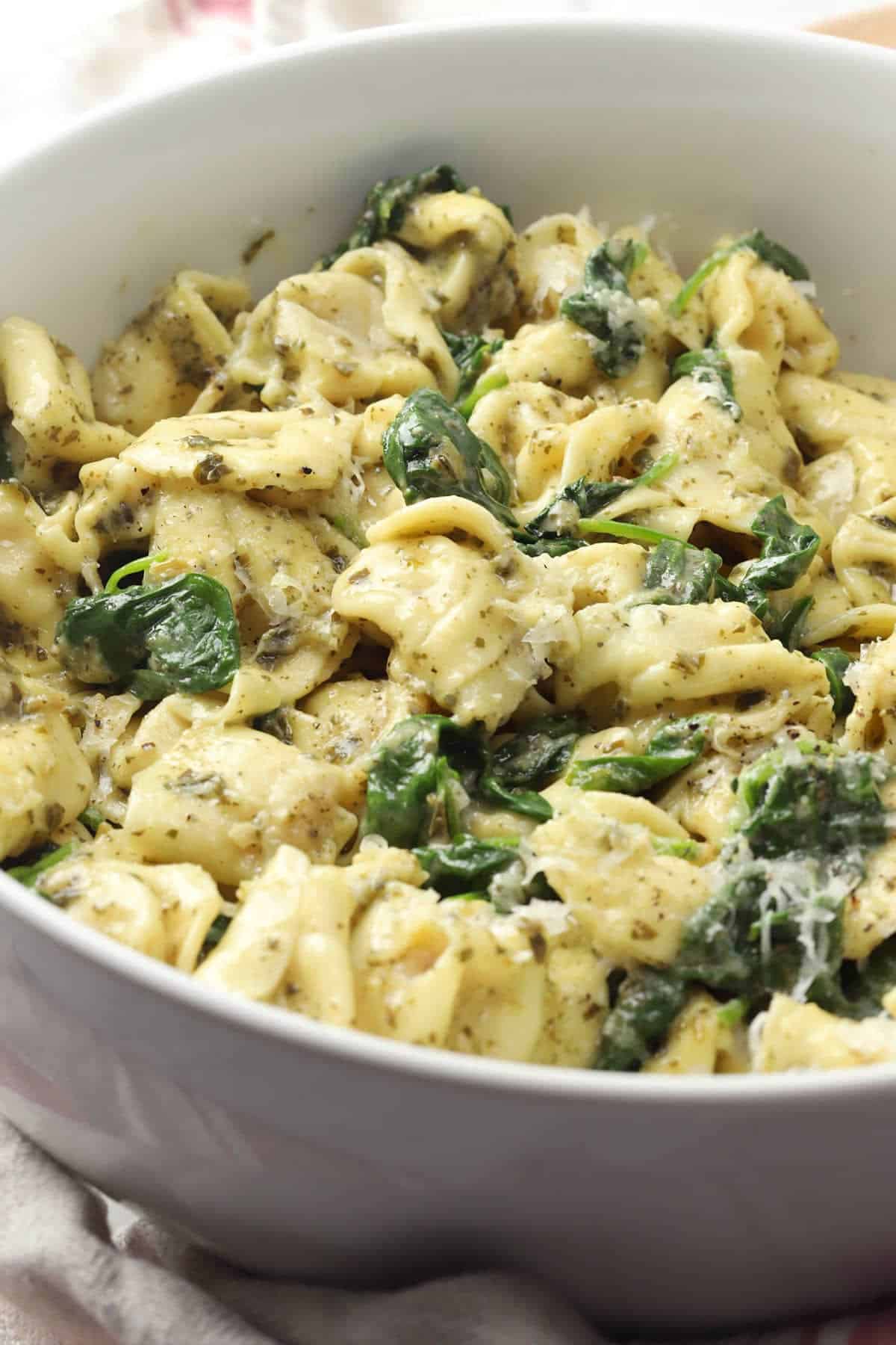 A bowl of spinach and tortellini in a creamy sauce.