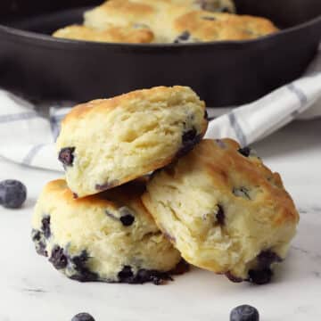 Three blueberry biscuits stacked on a counter top.