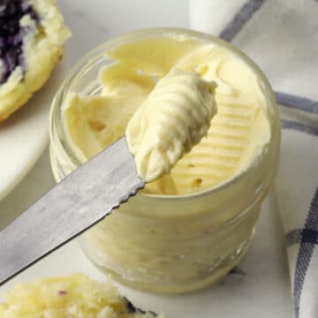 A knife with a serving of whipped honey butter over a glass jar.