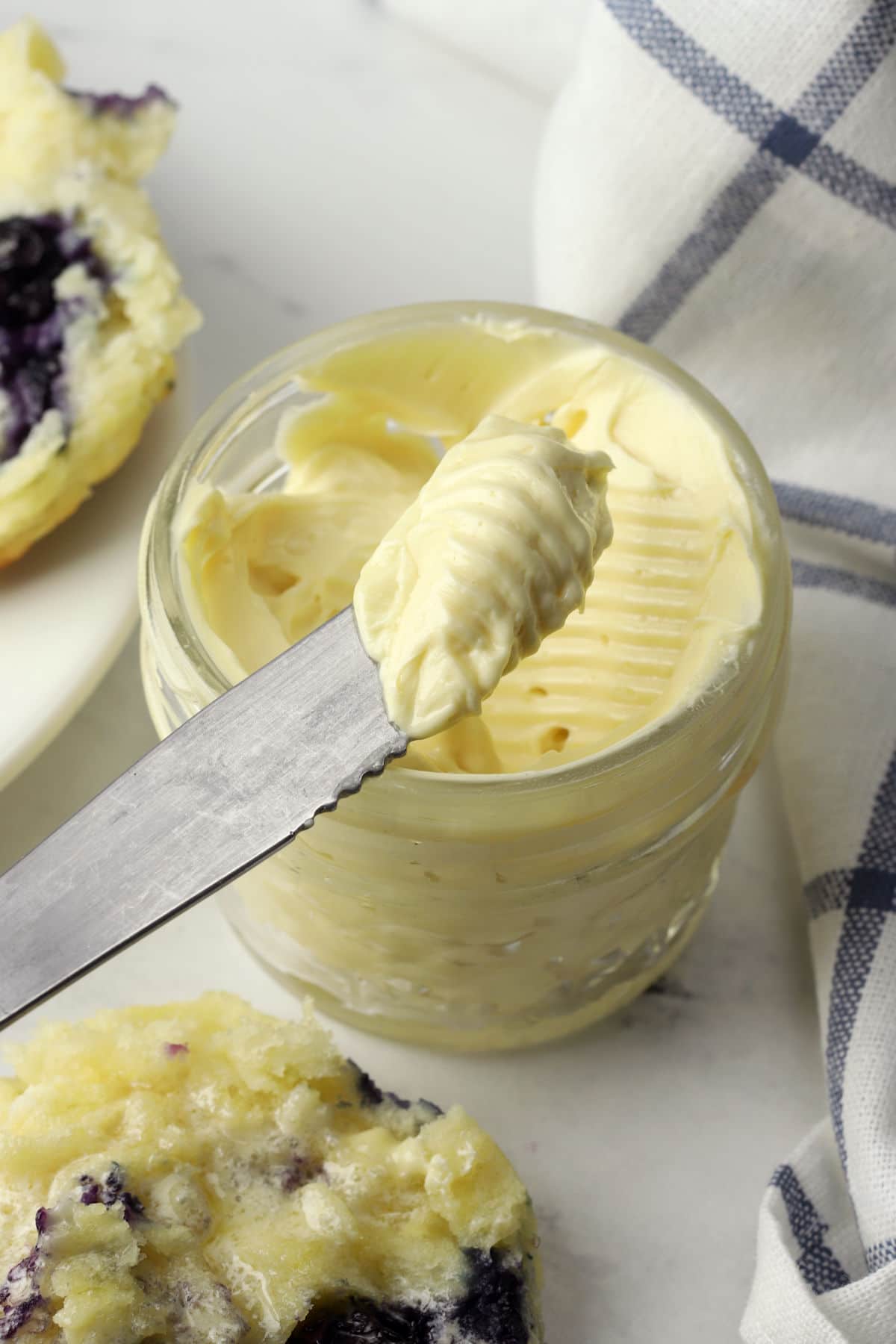 A knife with a serving of whipped honey butter over a glass jar.