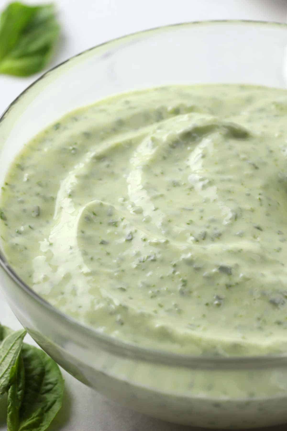 Close up of creamy aioli with flecks of basil in a glass bowl.