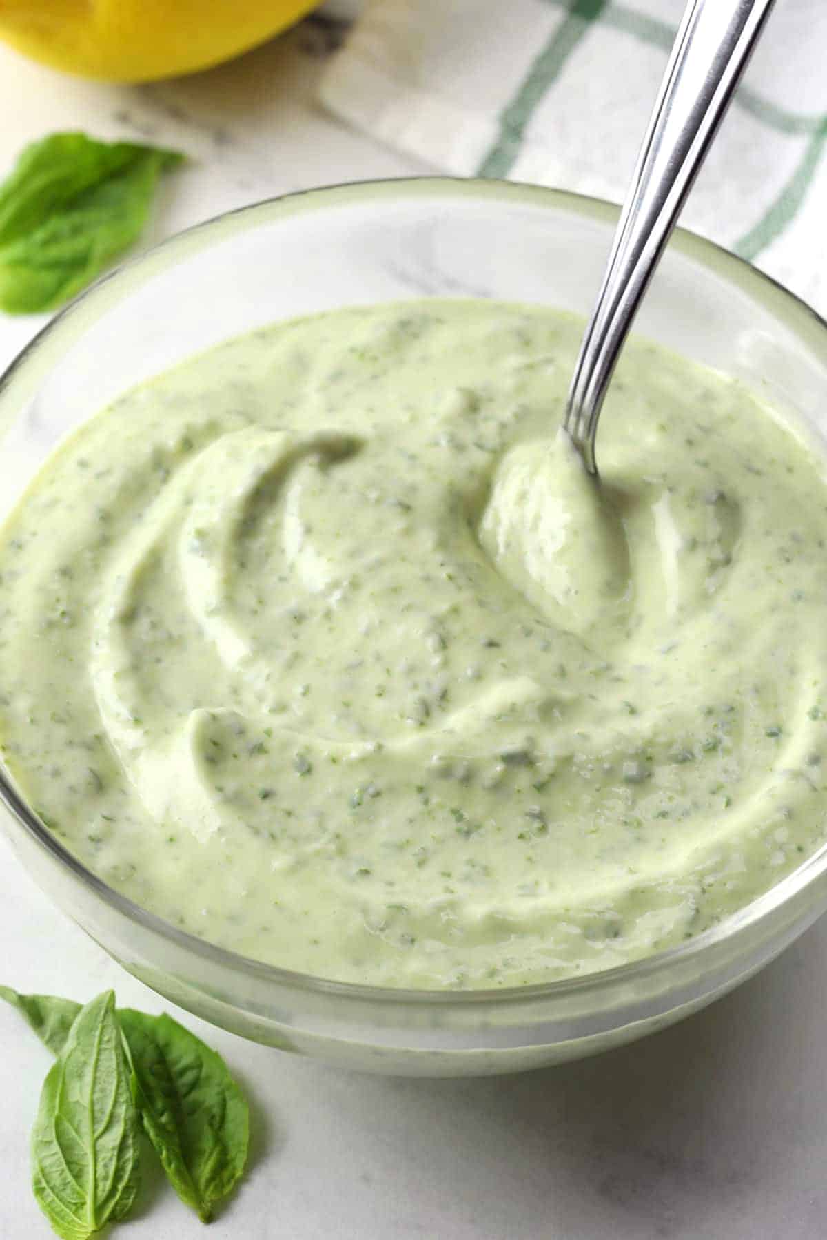 A glass bowl filled with basil aioli with a metal spoon.