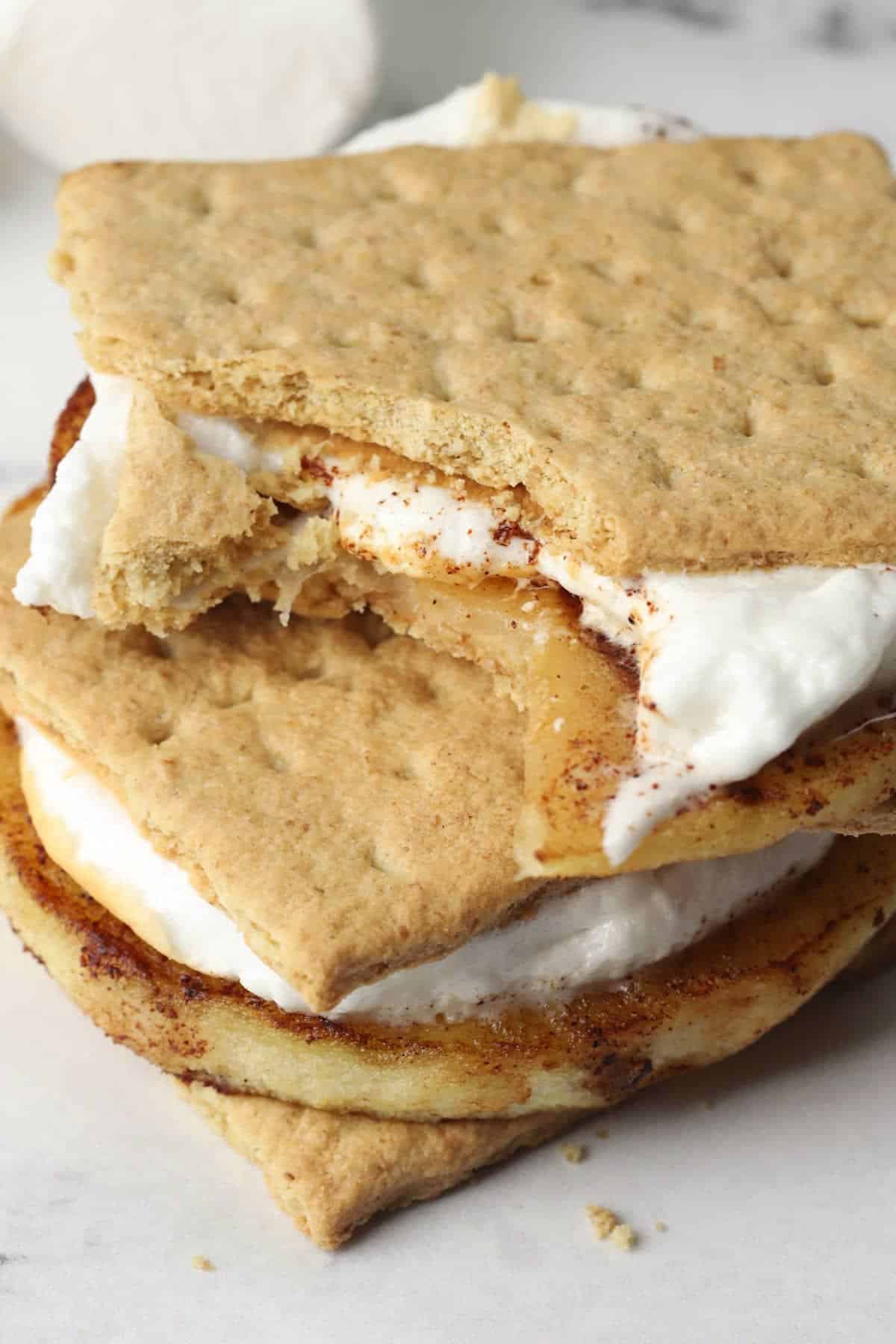 Two stacked grilled apple s'mores with one missing a bite.