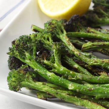 Close up of grilled broccolini stalks on a plate with a lemon wedge.