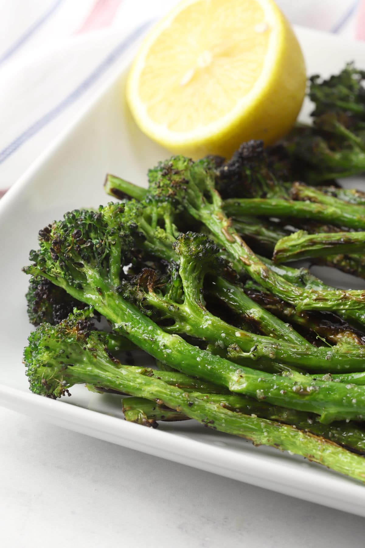 Close up of grilled broccolini stalks on a plate with a lemon wedge.