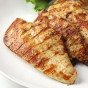 Close up of grilled lemon pepper chicken breast on a white plate.