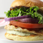 Grilled lemon pepper chicken sandwich stacked with lettuce, onion, and tomato on a white plate.