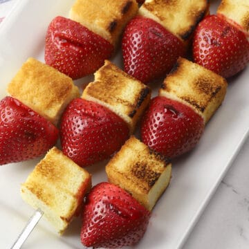 Grilled strawberry shortcake kebabs on a white serving plate.