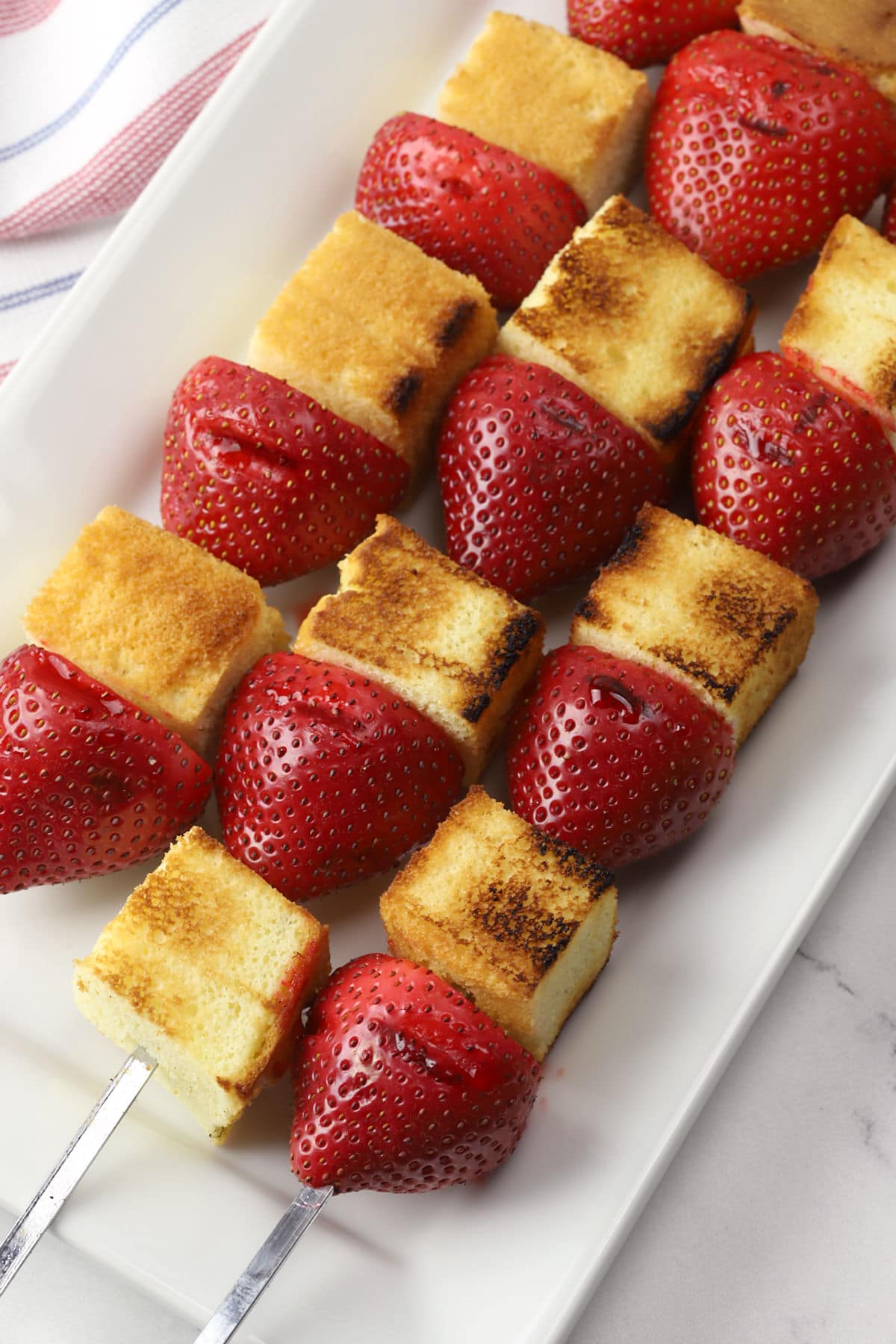 Grilled strawberry shortcake kebabs on a white serving plate.