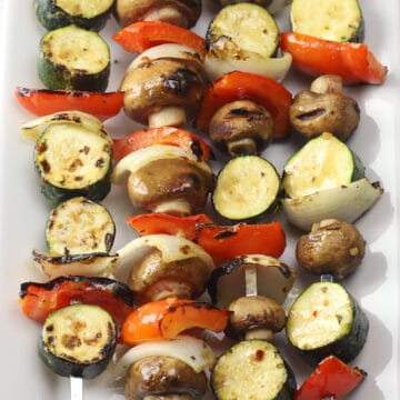Four skewers filled with sliced zucchini, onions, peppers, and mushrooms.