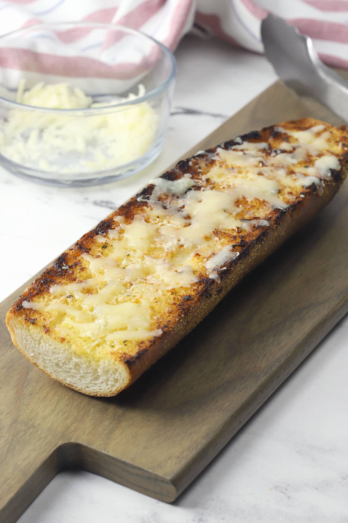 A whole piece of garlic bread with grill marks, placed on a wooden cutting board.