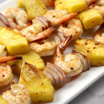 Close up of grilled pineapple, onion, and shrimp on a metal skewer.