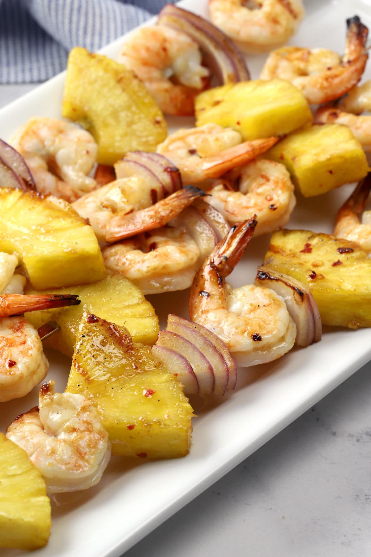 Close up of grilled pineapple, onion, and shrimp on a metal skewer.