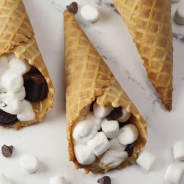 Waffle cones filled with melted marshmallows and chocolate chips laying on a counter top.