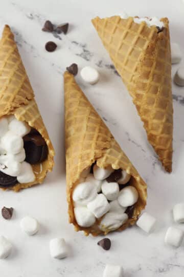 Waffle cones filled with melted marshmallows and chocolate chips laying on a counter top.