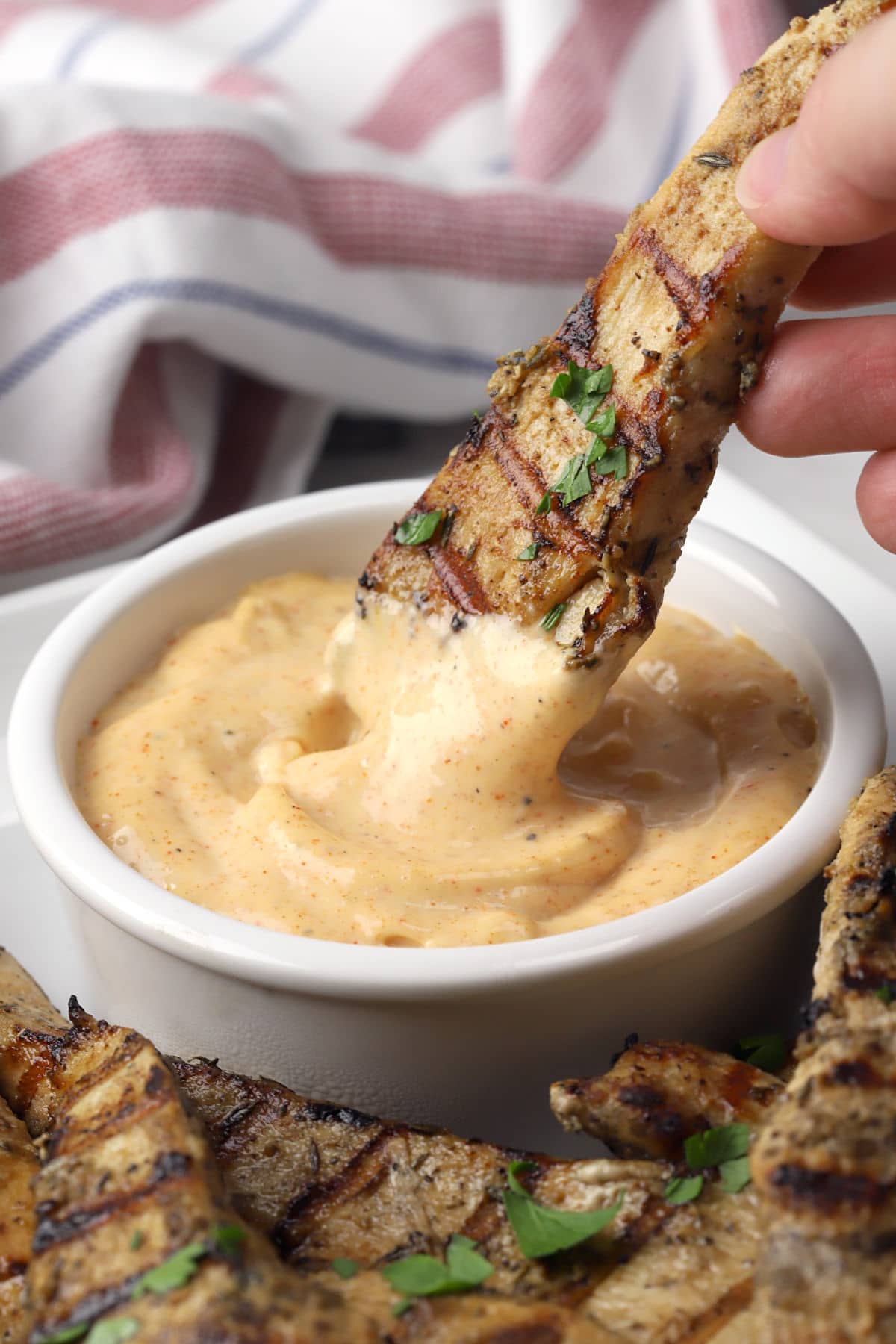 Chicken tender being dipped into a bowl of spicy aioli.