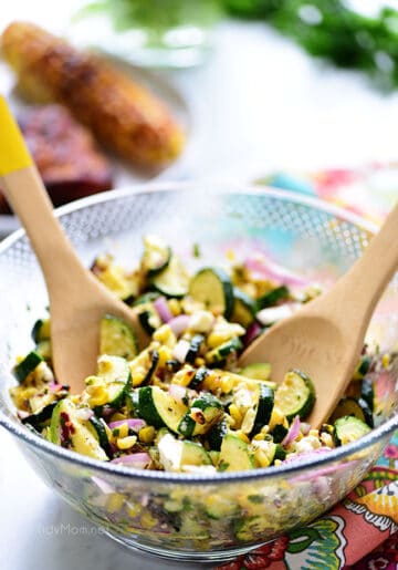 Grilled corn and zucchini salad in a glass bowl with wooden serving spoons.