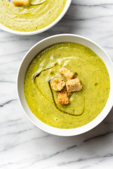 Two bowls filled with creamy zucchini soup, topped with croutons.