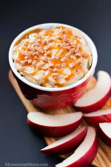 Red bowl filled with caramel dip with sliced apples.