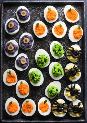 Deviled eggs topped with Halloween decorations like olive spiders and eyeballs.