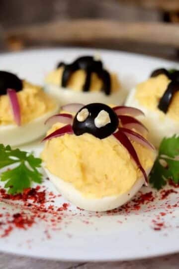 Deviled eggs with decorative spiders on top made of olives and onions.