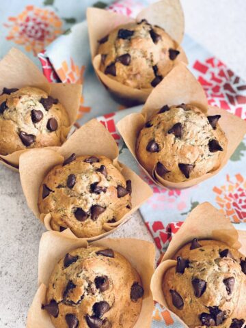 zucchini chocolate chip muffins with brown parchment liners on a floral towel.