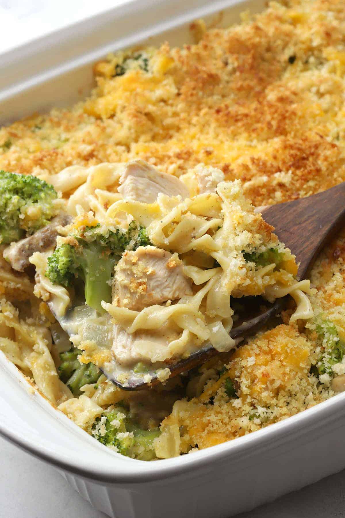 Wooden server scooping turkey broccoli casserole from a dish.