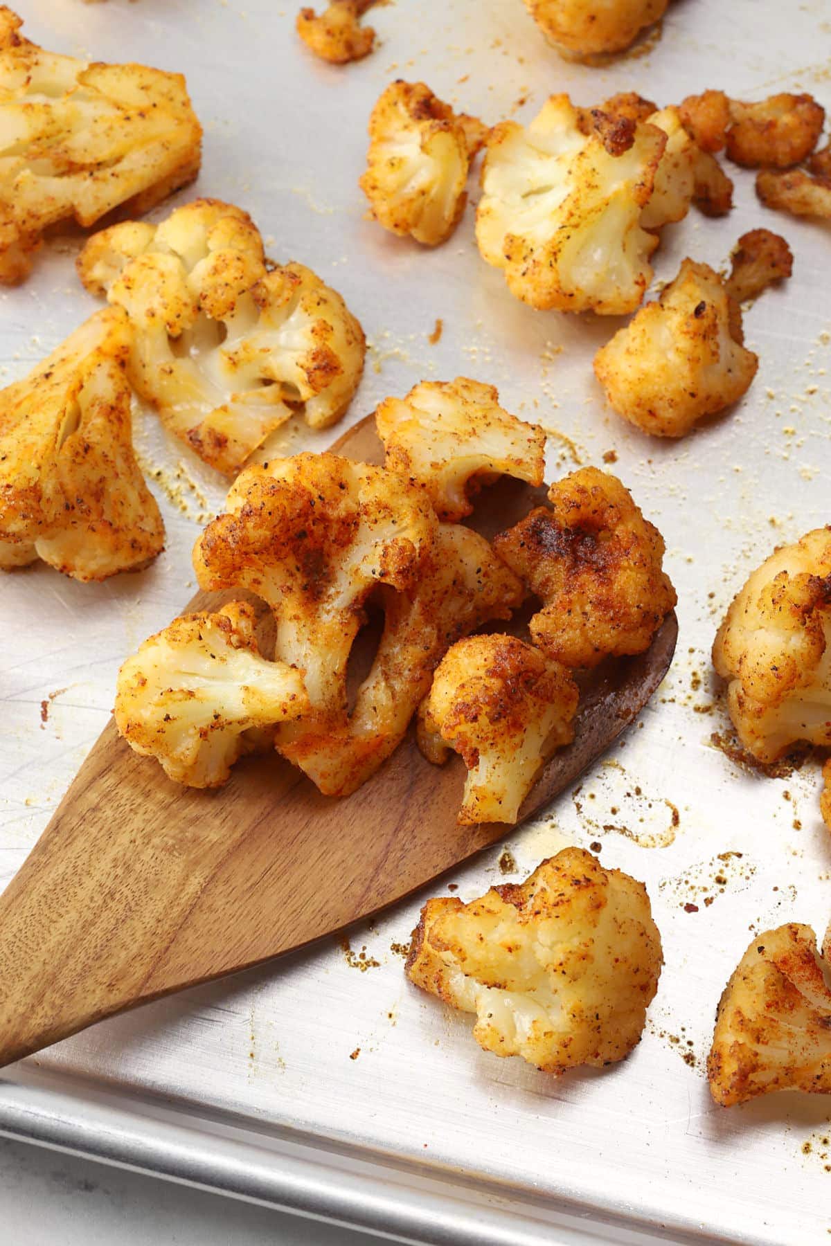 Wooden spatula scooping roasted cauliflower from a sheet pan.
