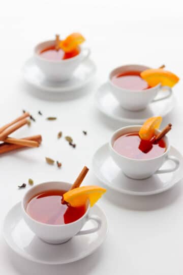 Teacups filled with orange tea, cinnamon sticks, and orange slices.