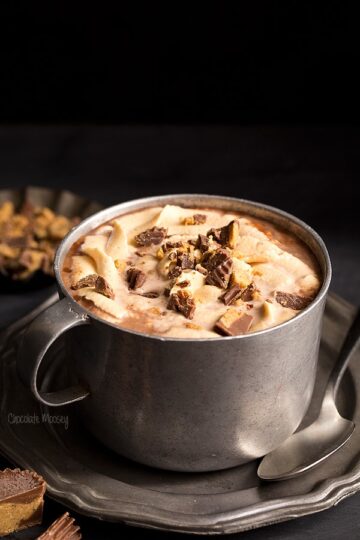 A metal mug filled with peanut butter hot chocolate that's topped with chopped peanut butter cups.