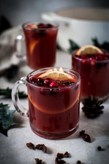 Glass mugs filled with warm homemade wassail, topped with cranberries and orange slices.
