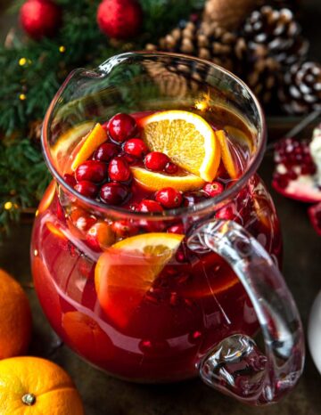 A glass pitcher filled with red punch and sliced fruit.