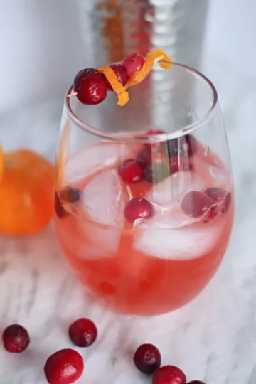 A red cocktail in a glass with ice and cranberries.