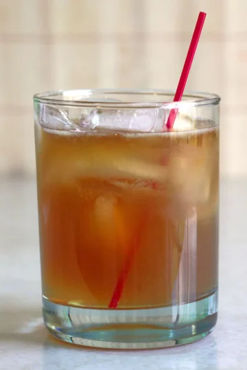 Lowball glass with ice and a red stirrer, filled with a brown cocktail.