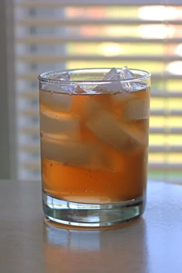 A brown cocktail in a lowball glass with ice.