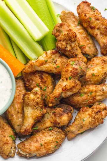 Air fryer chicken wings with celery and carrots on a serving plate.
