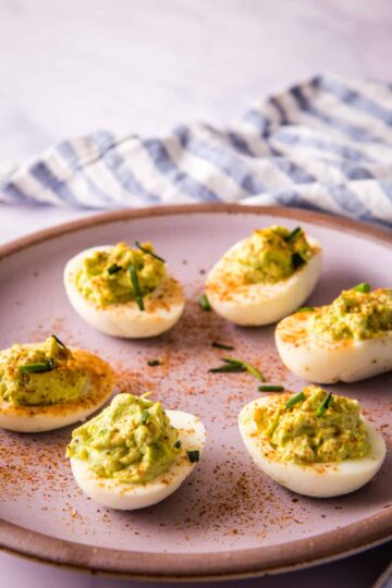 Avocado deviled eggs garnished with paprika and chives on a serving plate.
