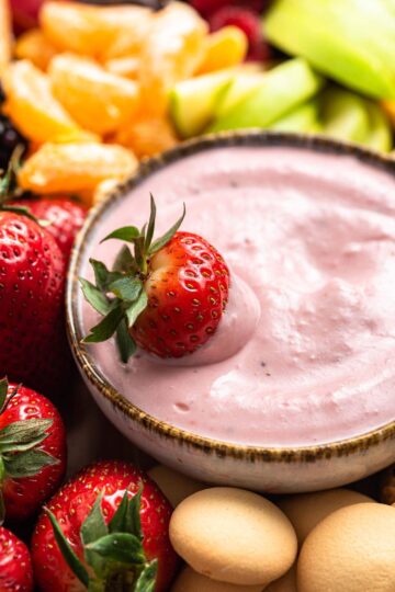 Bowl of pink fruit dip with a strawberry.