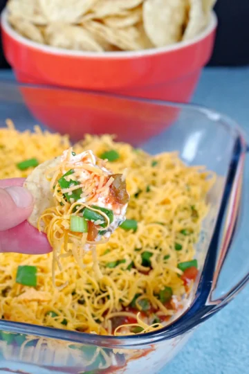 A hand grabbing a chip topped with layered taco dip.